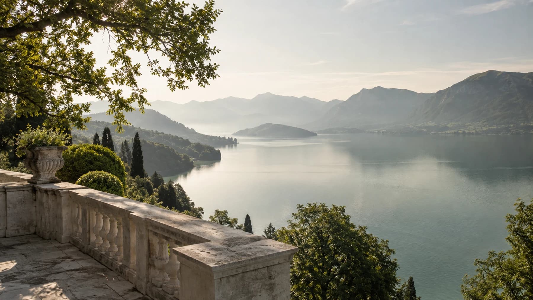 A calm lake and distant hills framed by trees and a stone terrace
